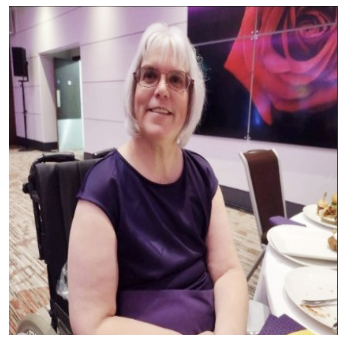 A woman in a dark purple top and glasses smiling at a dining table during an indoor event.